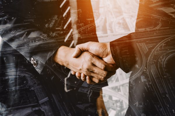 Double exposure image of business people handshake on city office building in background showing partnership success of business deal. Concept of corporate teamwork, trust partner and work agreement.